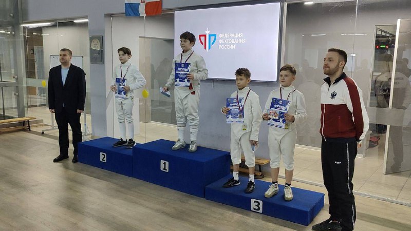 14 февраля 2026 года в Екатеринбурге прошел традиционный открытый турнир по фехтованию на саблях, собравший юных спортсменов со всей России. Одним из главных героев соревнований стал ученик 5-го класса Даниил Кадышев, выступавший в составе команды «Пермь-I». Даниил занял 1-е место среди мальчиков 12 лет ! Даниил, занимаясь всего два года в Пермском центре фехтования, смог значительно увеличить интенсивность своей подготовки, перейдя с трех тренировок в неделю на пять. Такой подход позволил юному спортсмену существенно повысить свое мастерство и добиться отличных результатов на соревнованиях.Помимо физической подготовки, занятия фехтованием способствуют развитию важных личностных качеств. Умение сохранять хладнокровие даже в условиях высокого давления, уважение к сопернику и умение достойно воспринимать любые исходы матчей – всё это делает фехтовальщика настоящим мастером своего дела.Поздравляем Даниила и всю команду «Пермь-I» с заслуженной победой и желаем новых спортивных достижений!